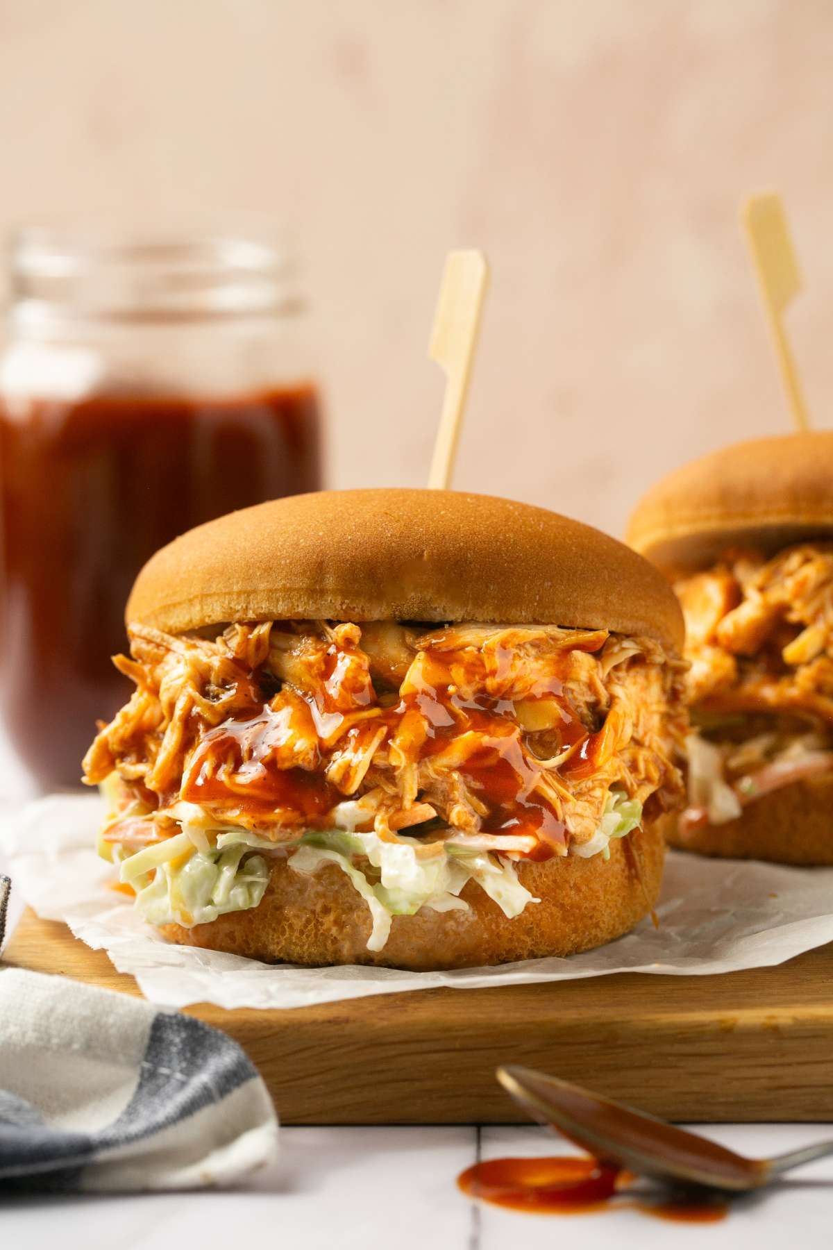 A shredded bbq chicken crock pot sandwich on the table with coleslaw and a spoon dripping bbq sauce on the side.