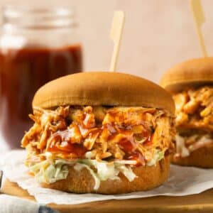 Shredded BBQ chicken crockpot served on a bun with a jar of bbq sauce in the background.