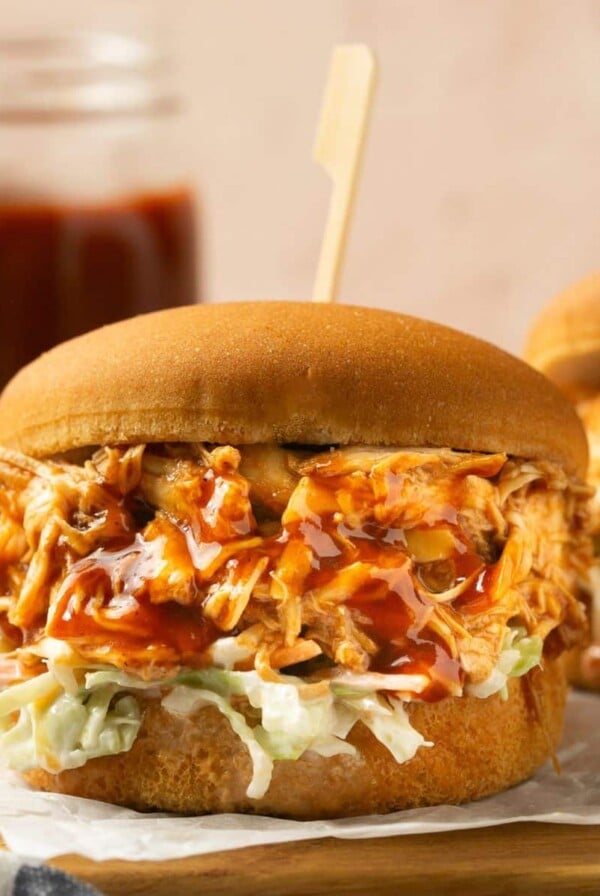 Shredded BBQ chicken crockpot served on a bun with a jar of bbq sauce in the background.