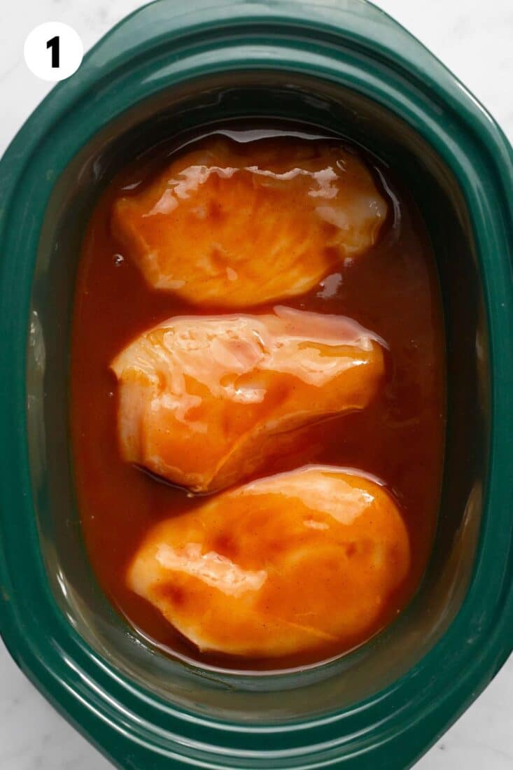 Chicken breasts and barbecue sauce in a slow cooker.