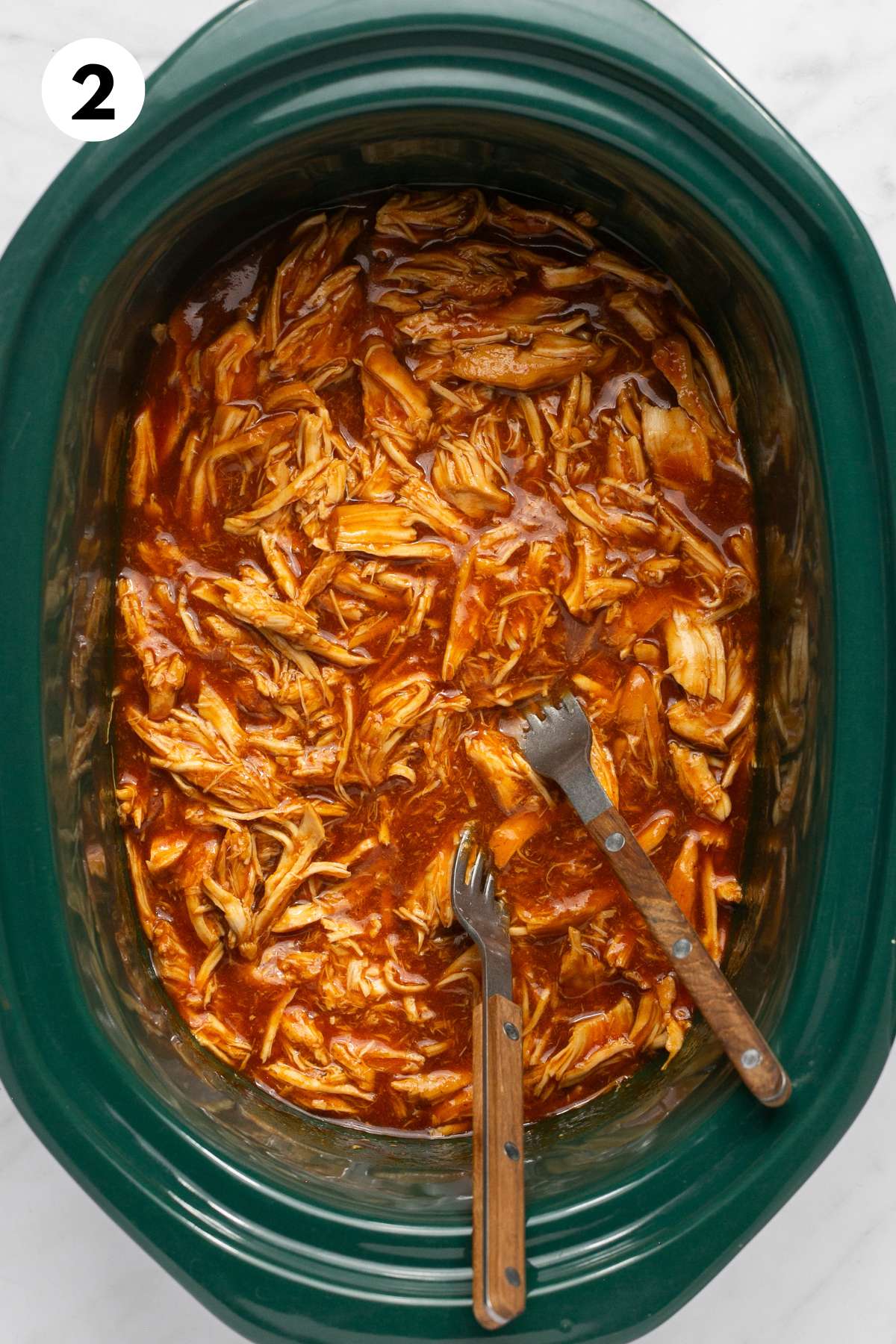 BBQ shredded chicken in the crockpot with two forks.