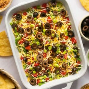 Taco dip in a rectangle baking dish surrounded by tortilla chips.