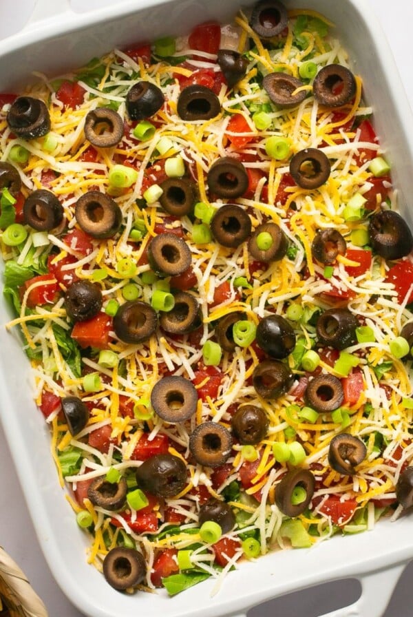 Taco dip in a rectangle baking dish surrounded by tortilla chips.