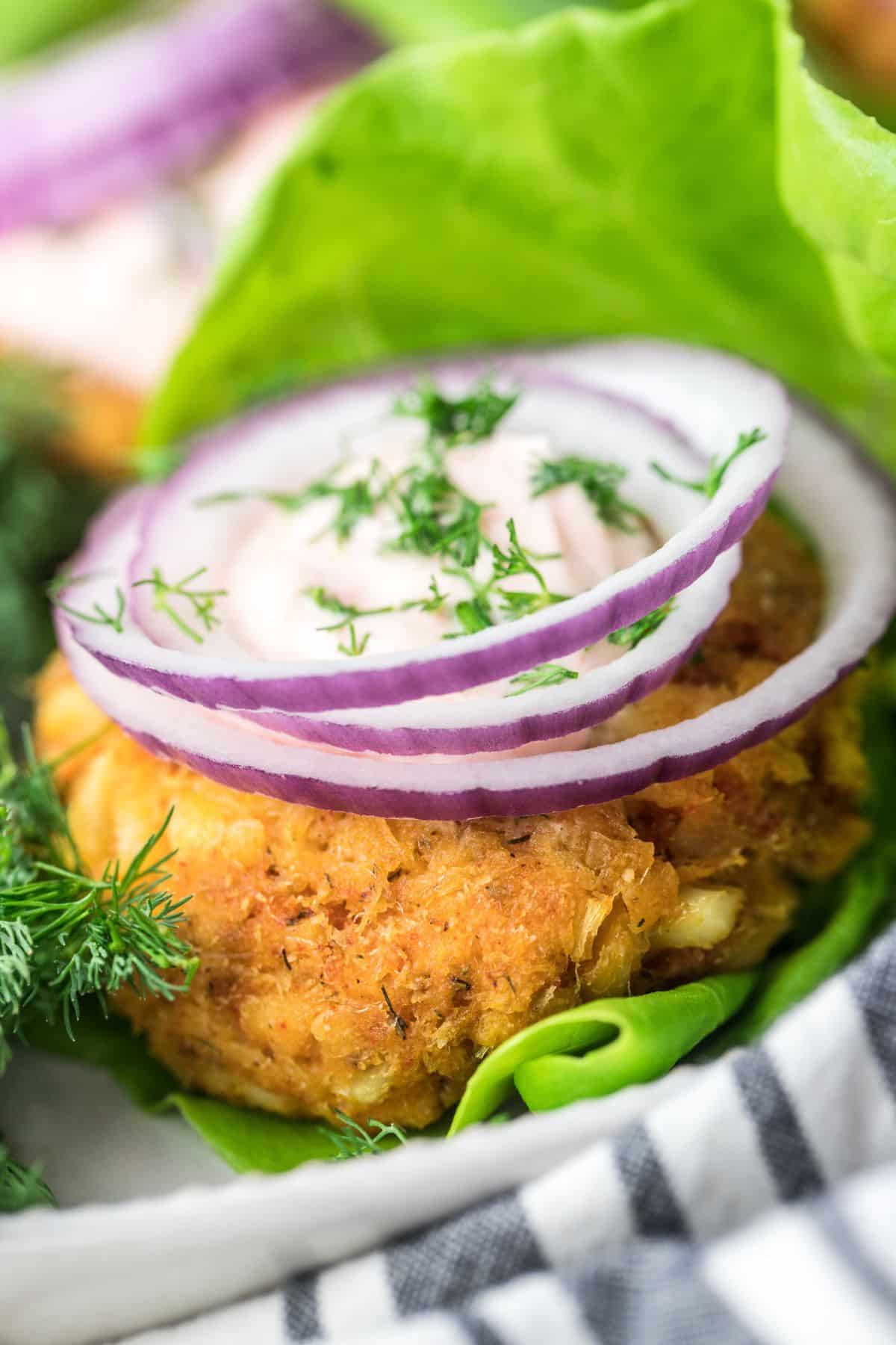 A healthy fish sandwich on a leaf of lettuce topped wit red onion slices, fresh dill and a sauce.