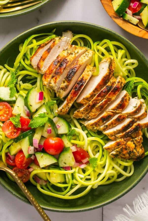 Greek chicken bowls on the table with a a wooden bowl of more salad to the side.