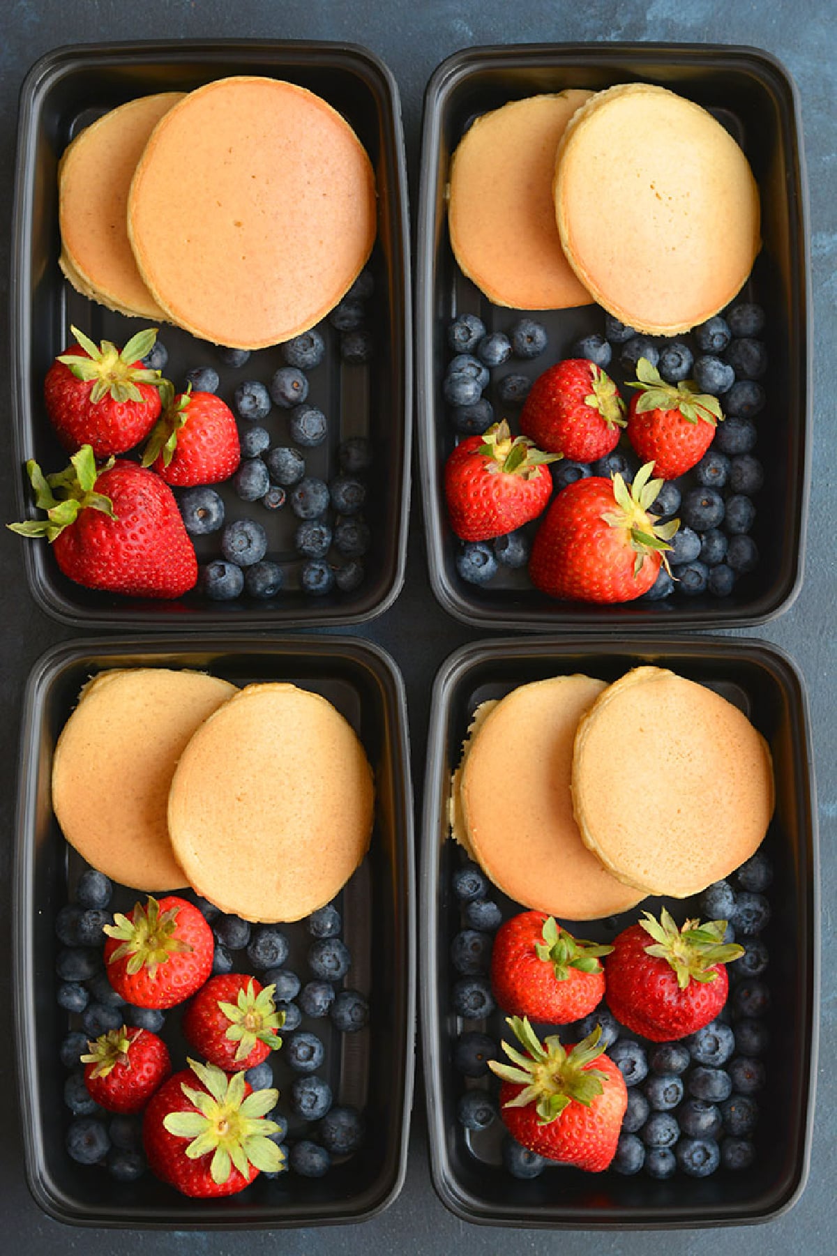 pancakes in a black meal prep container with blueberries and strawberries.