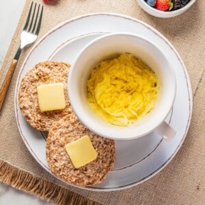 Microwave scrambled eggs in a mug with an english muffin topped with butter on the side.