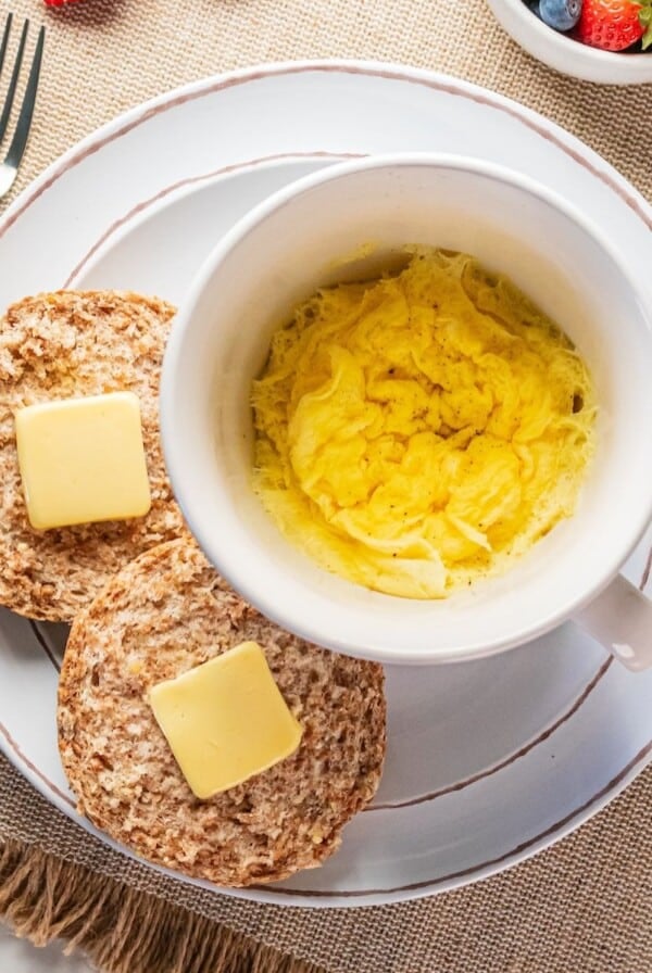 Microwave scrambled eggs in a mug with an english muffin topped with butter on the side.
