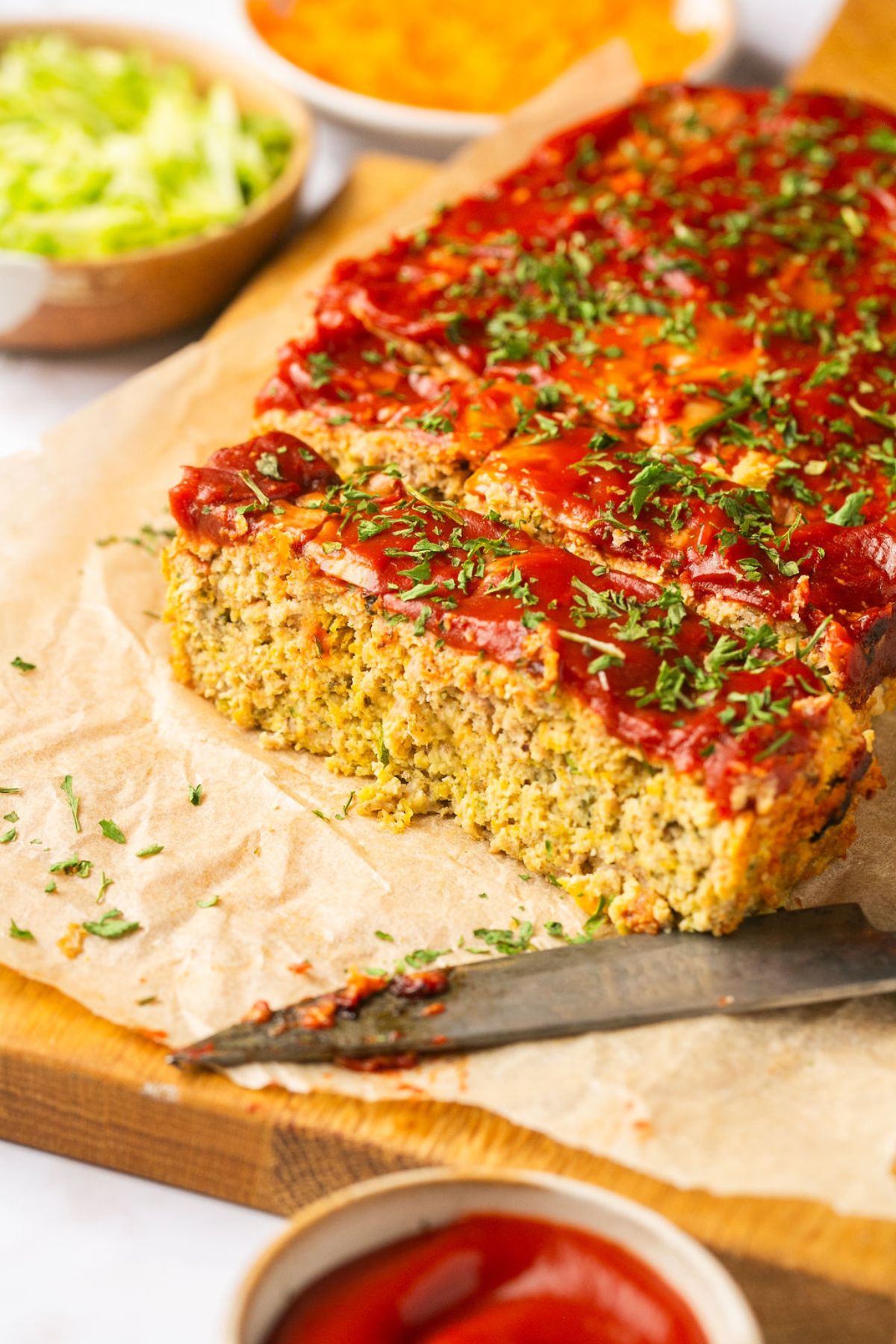 Paleo meatloaf on a piece of parchment on a cutting board sliced and a knife to the side.