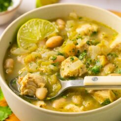 A bowl of healthy white chicken chili on the table with a lime and spoon.