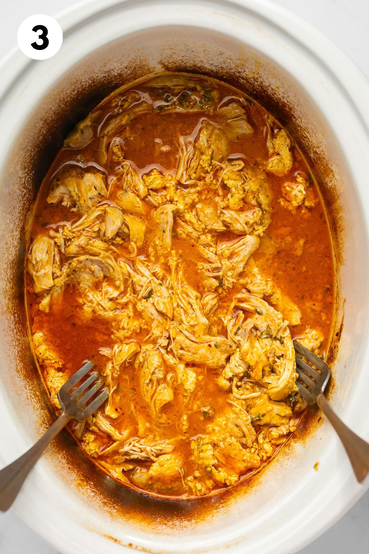 Chicken shredded in a crock pot with two forks to the side.