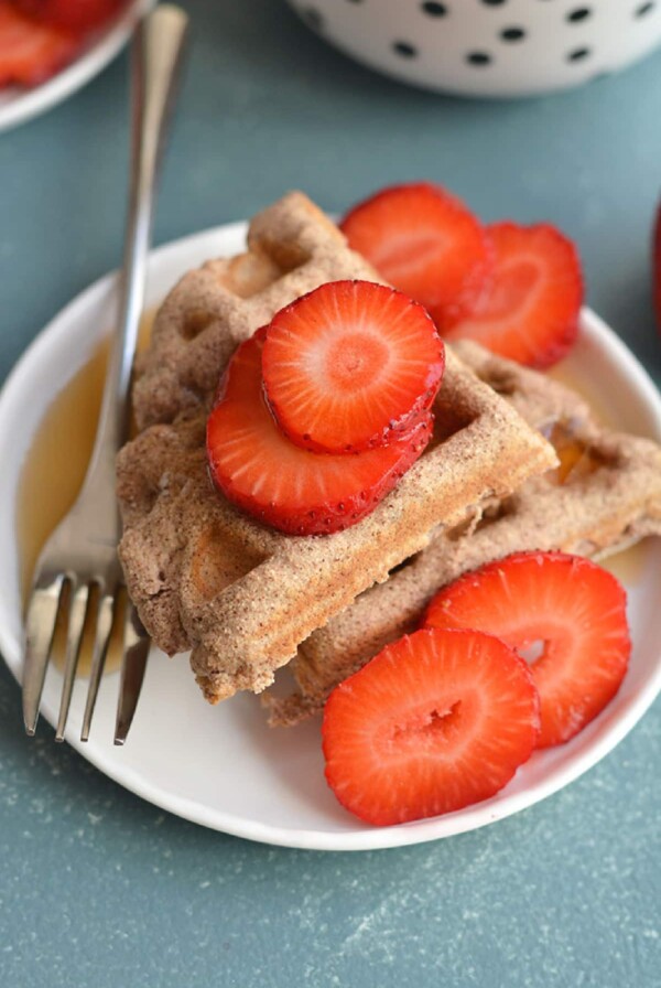 two waffles stacked on a white plate with a fork and sliced strawberries.