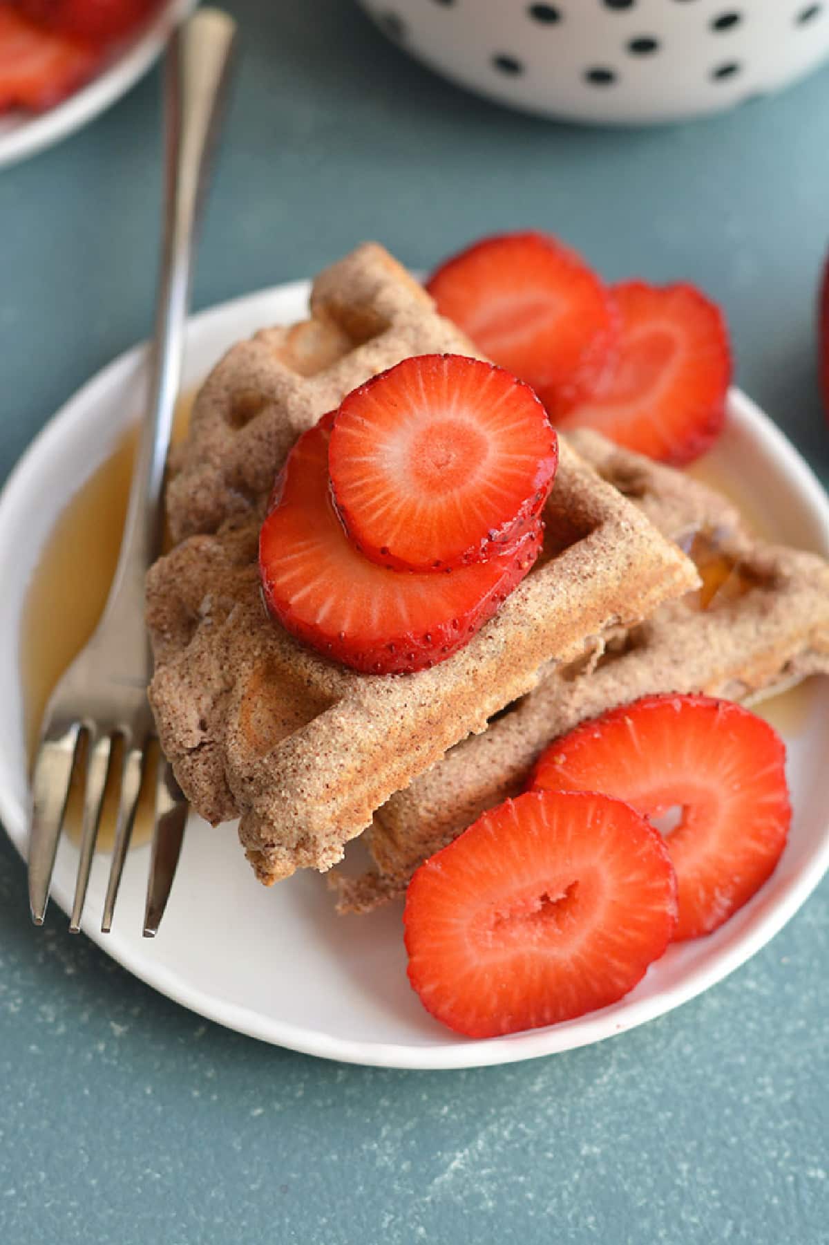 two waffles stacked on a white plate with a fork and sliced strawberries.