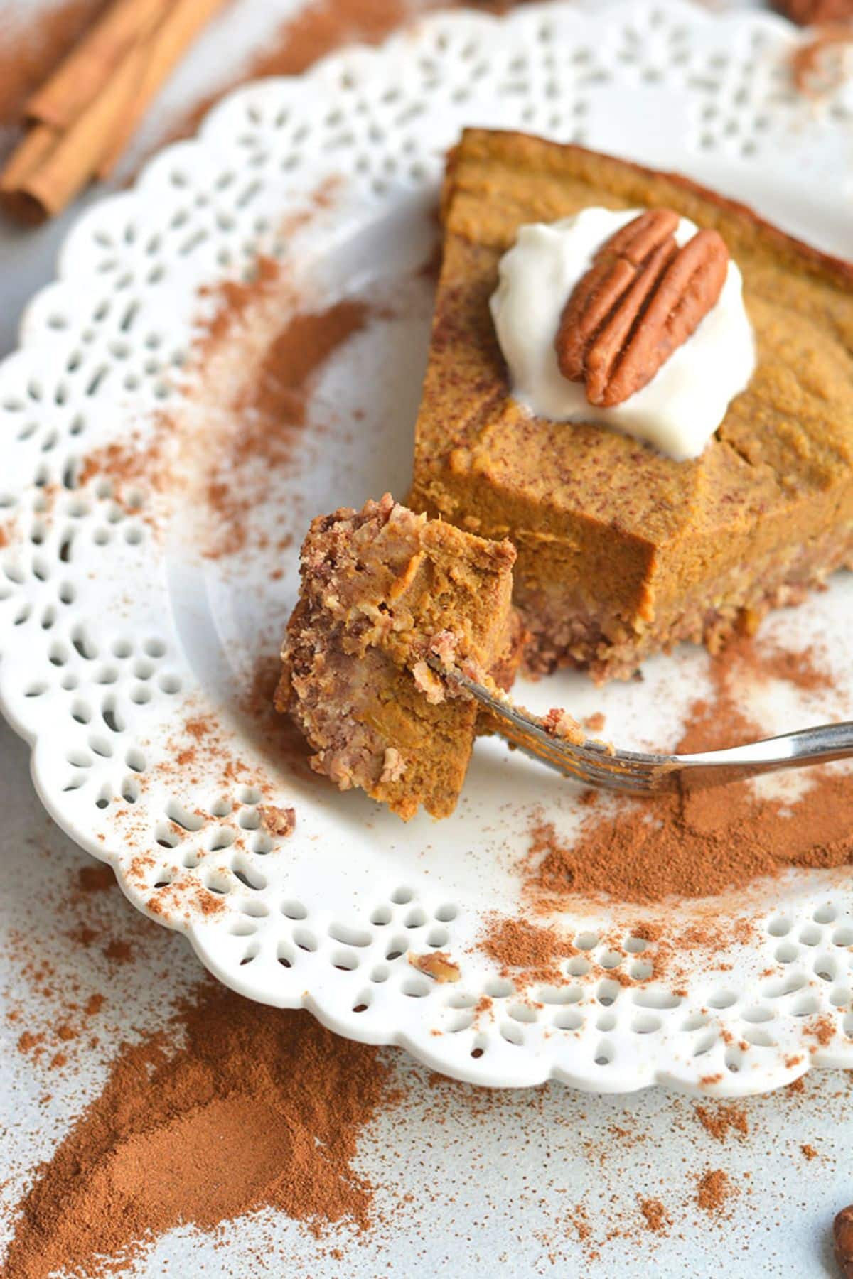 A slice of low calorie pumpkin pie on a white plate with a bite on a fork resting on the side.