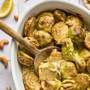 Brussels sprouts casserole on the table with a wooden spoon scooping some up.