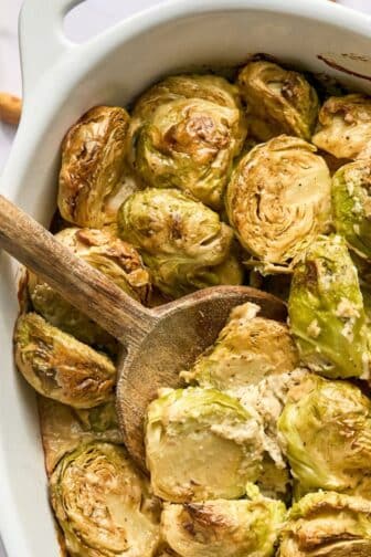 Brussels sprouts casserole on the table with a wooden spoon scooping some up.