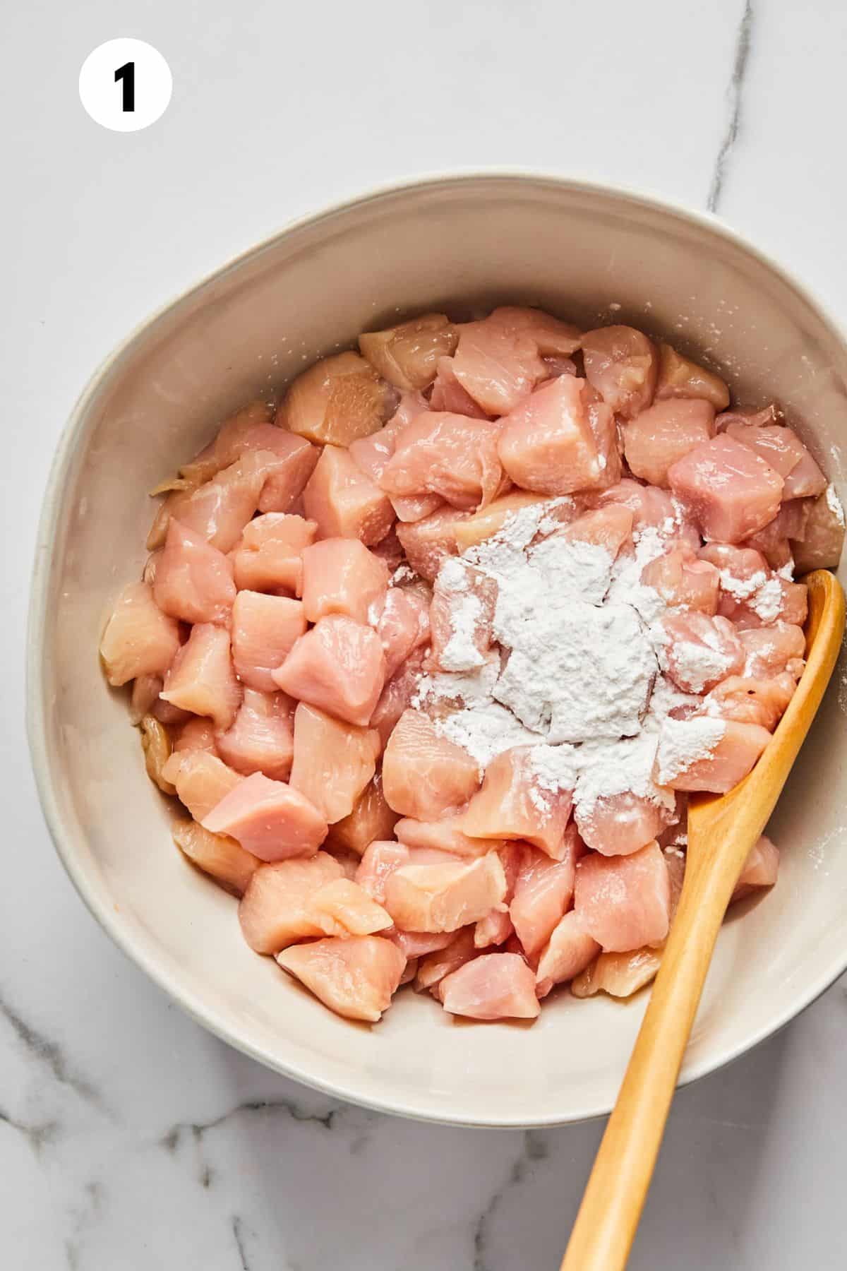 Cubed chicken being coated with cornstarch.