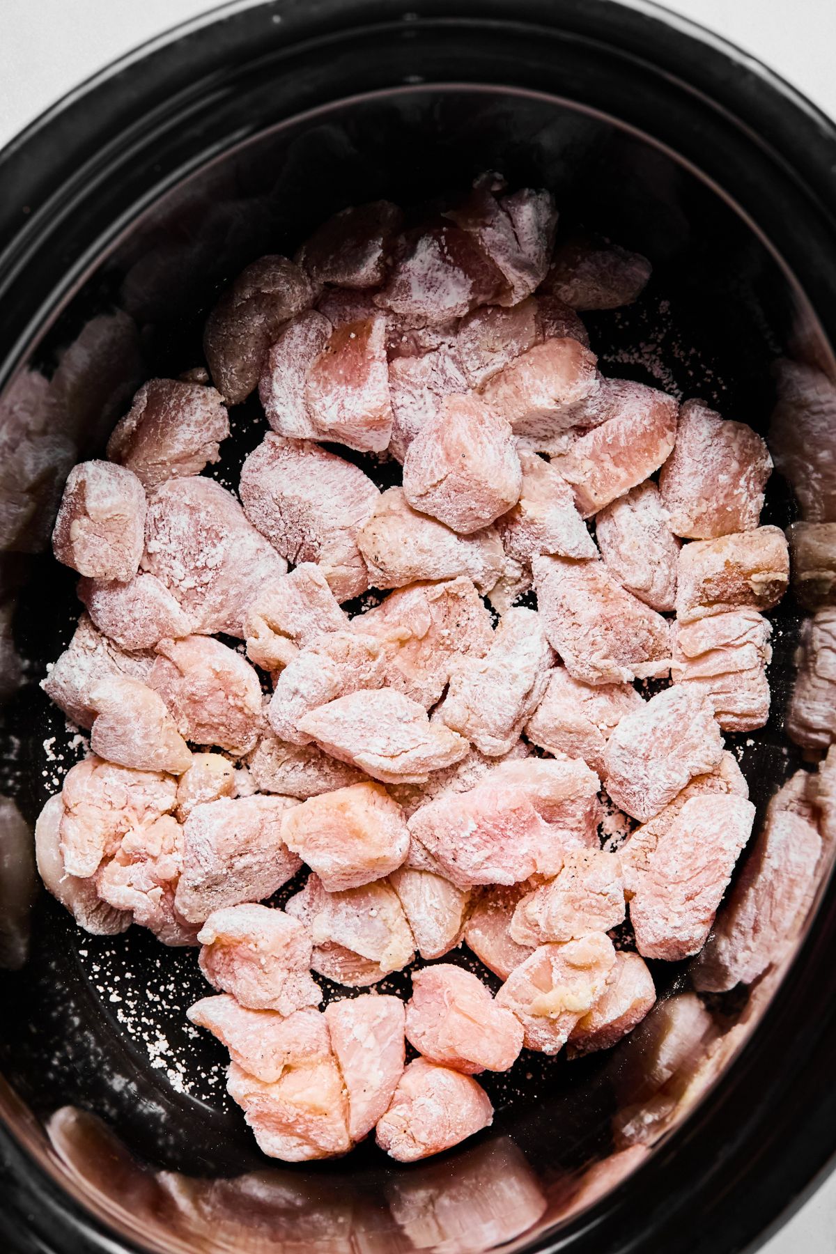 Chicken cubes added to a slow cooker.