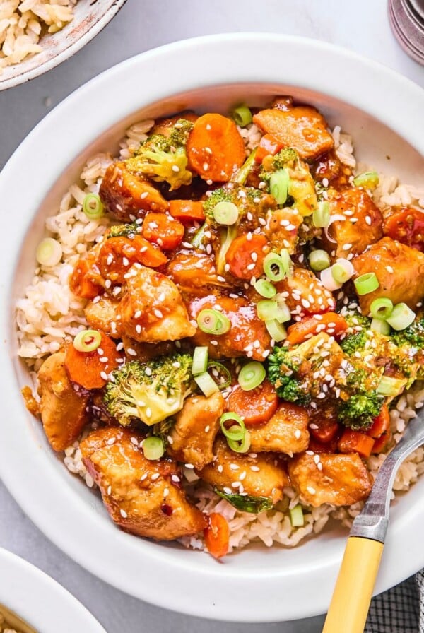A bowl full of mongolian chicken with a fork in the dish and sesame seeds on top.