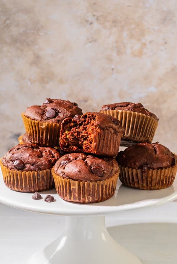 Chocolate avocado muffins on a cake plate with a bitten muffin on a plate on the table.