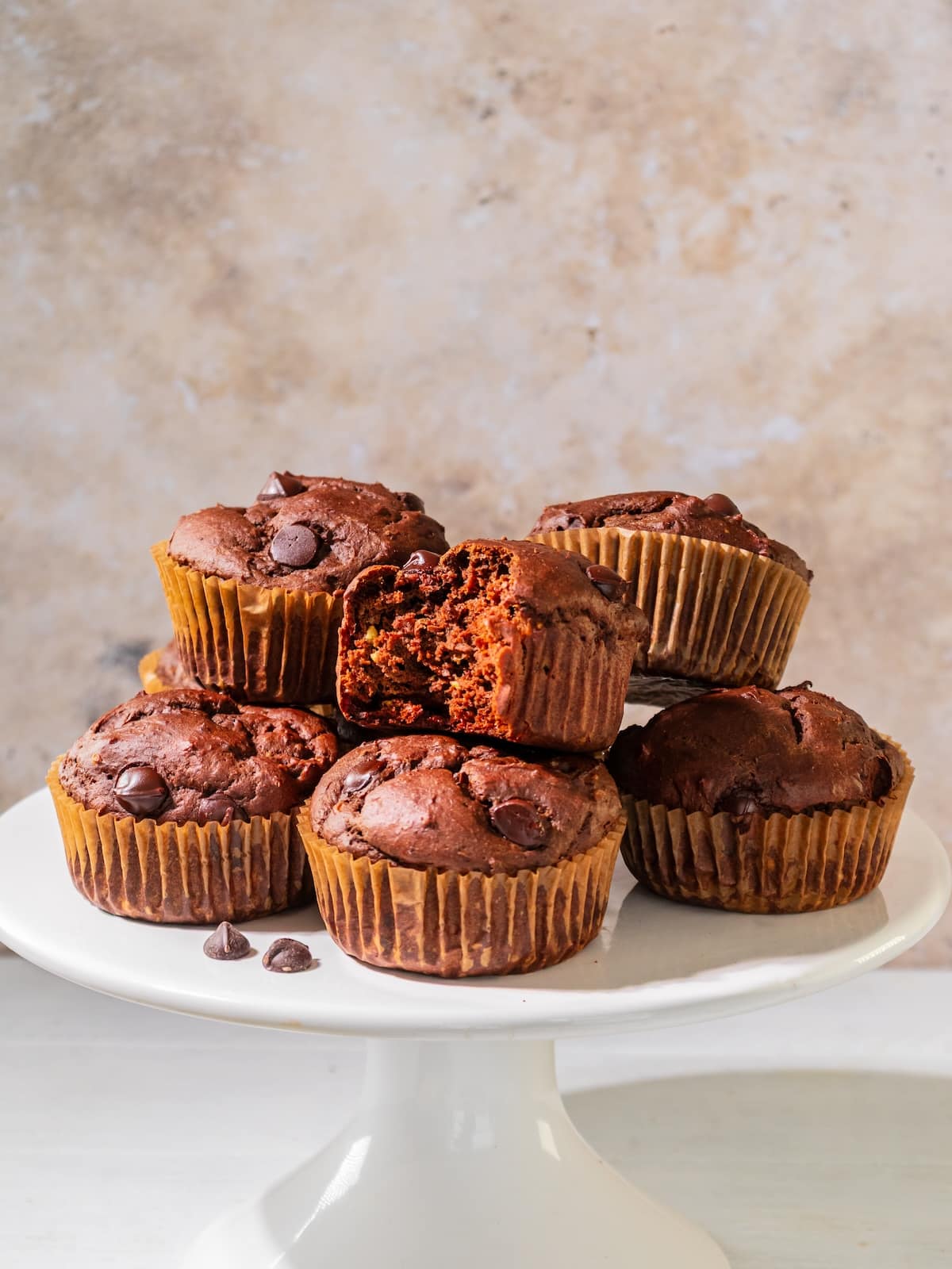 Chocolate avocado muffins on a cake plate with a bitten muffin on a plate on the table.