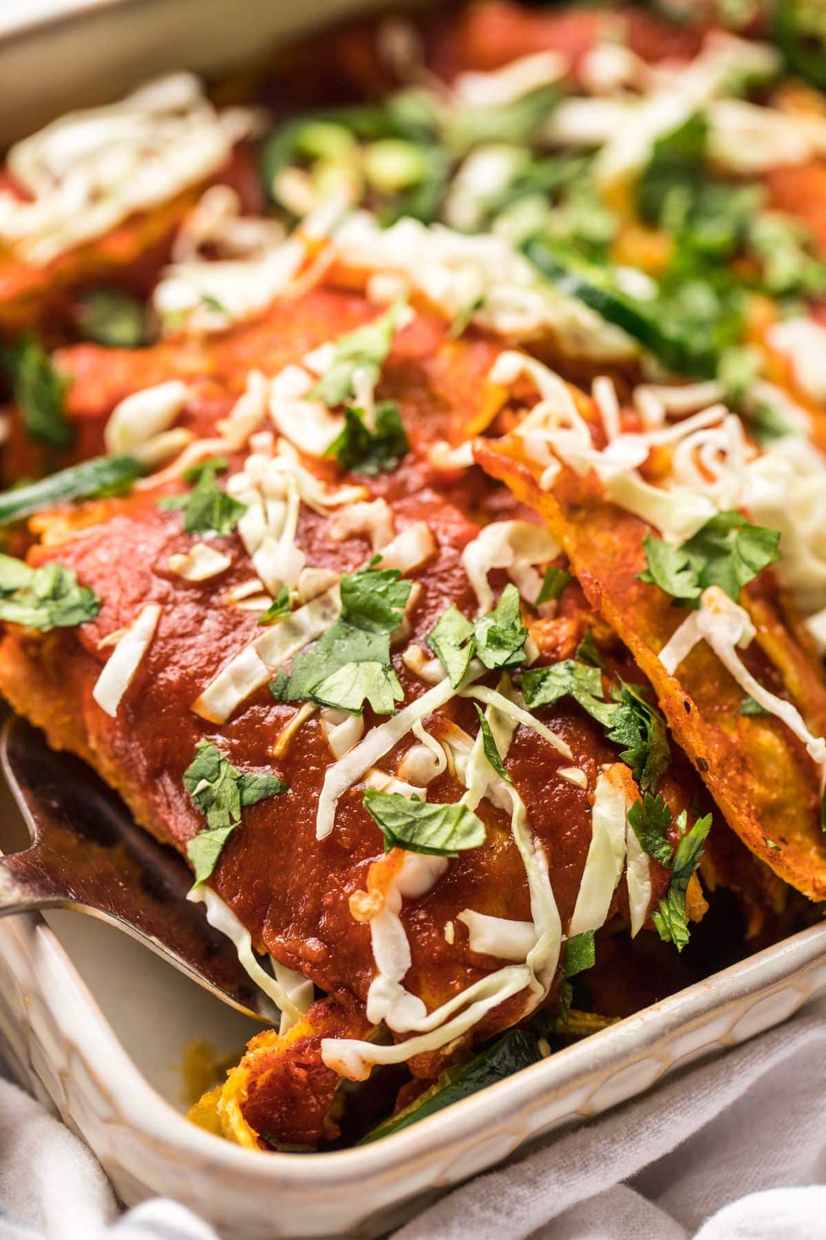 A casserole dish of healthy chicken enchiladas with a spatula scooping up a serving.