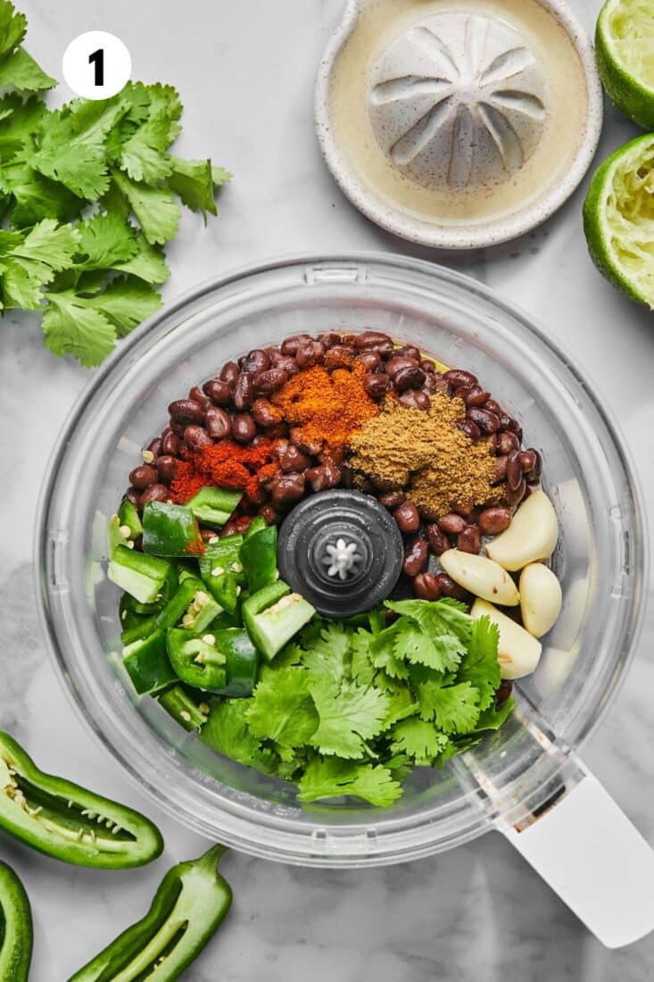 Ingredients to make black bean dip in a food processor bowl.