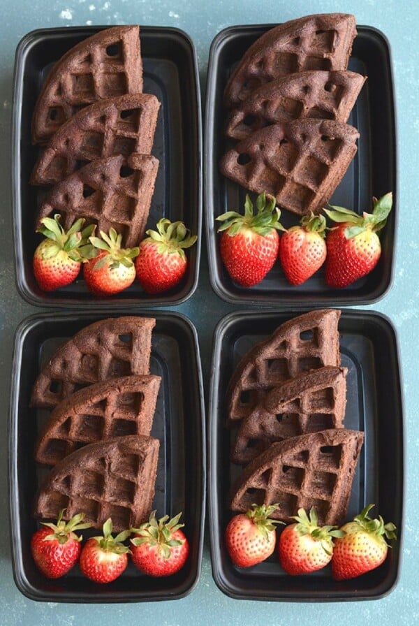 3 chocolate waffle quarters stacks in a meal prep container with strawberries.