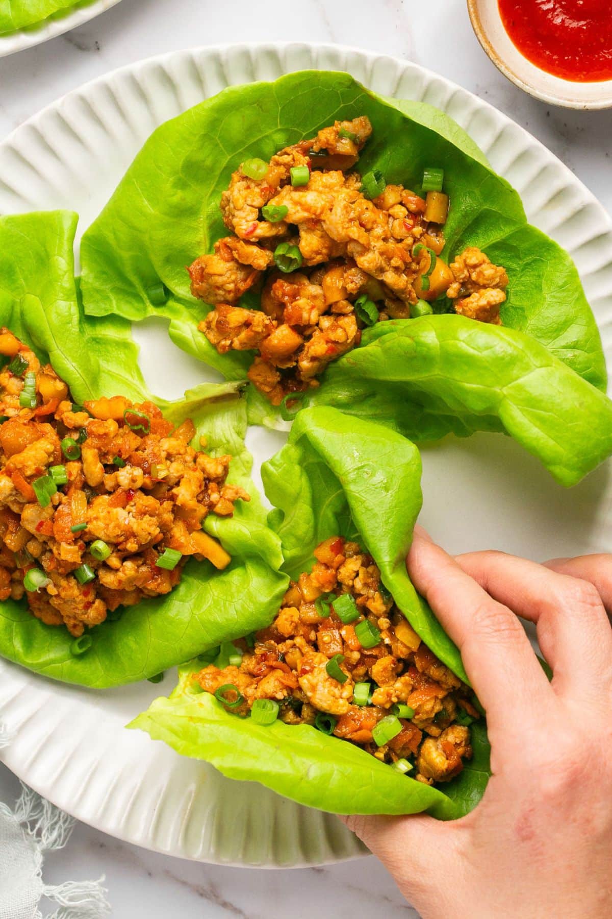 A hand reaching into grab a healthy chicken lettuce wrap from a plate on the table.