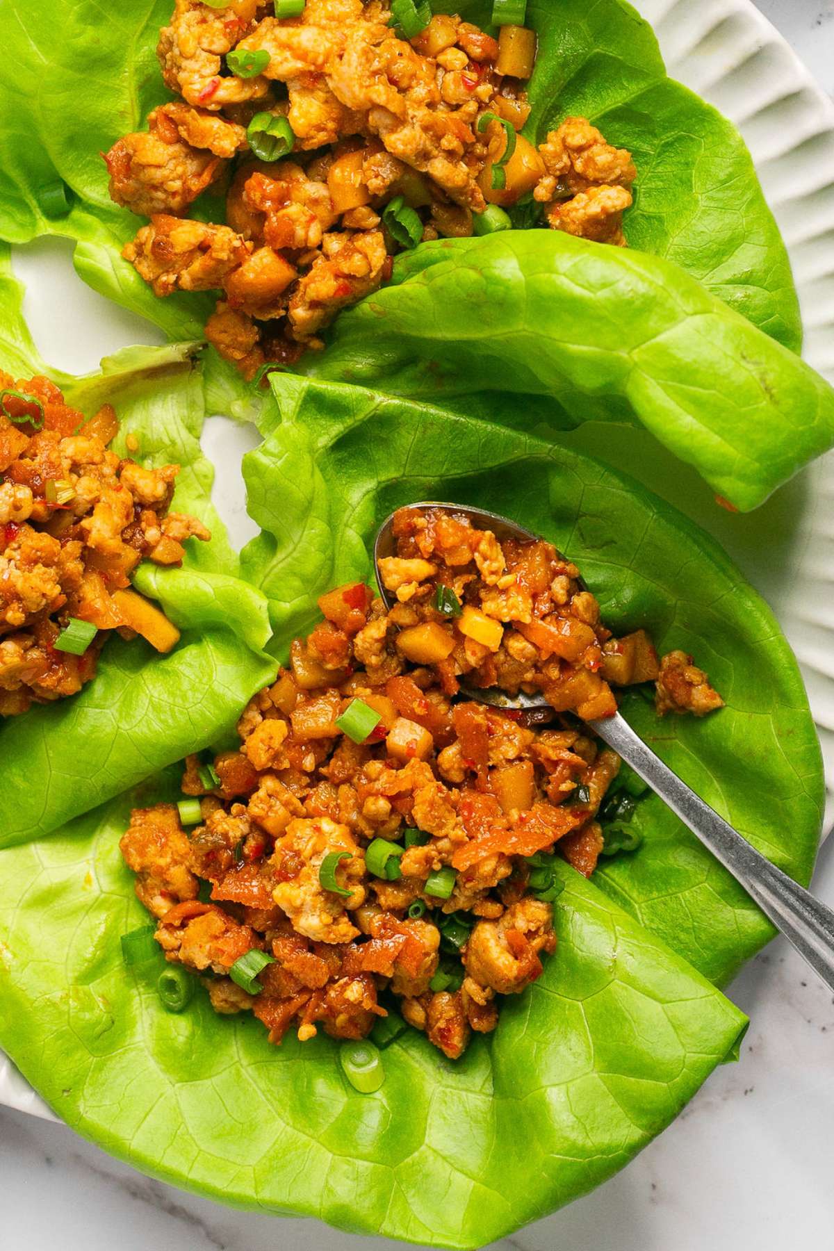 Ground chicken mixture scooped into lettuce cups with a spoon of it laying on the side. 