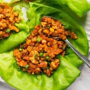 Healthy chicken lettuce wraps on a plate with a spoon of the filling to the side.