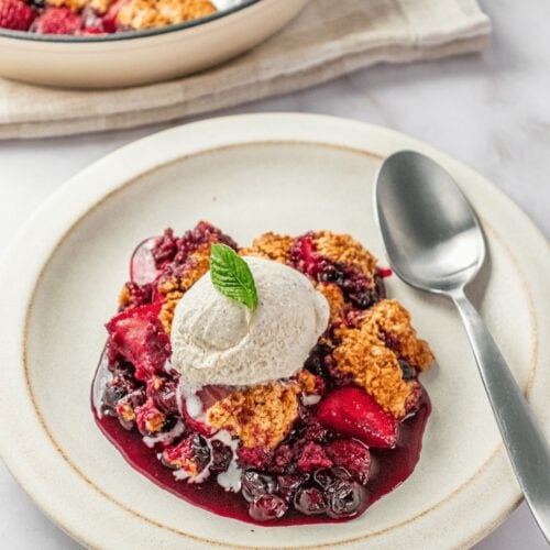 Gluten-free berry cobbler topped with whipped cream on a plate and a spoon to the side.