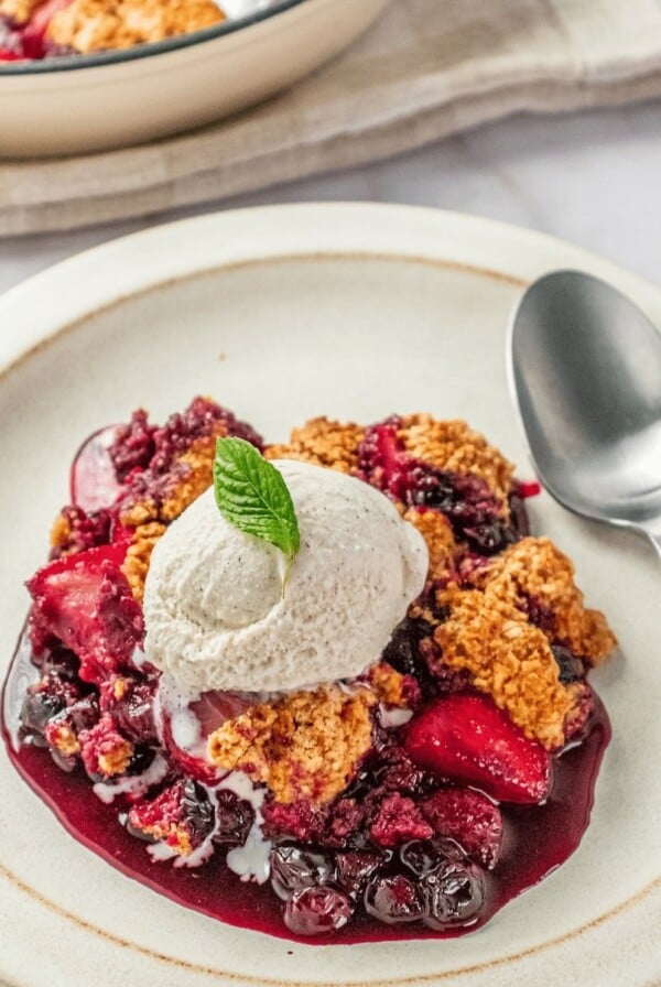 Gluten-free berry cobbler topped with whipped cream on a plate and a spoon to the side.