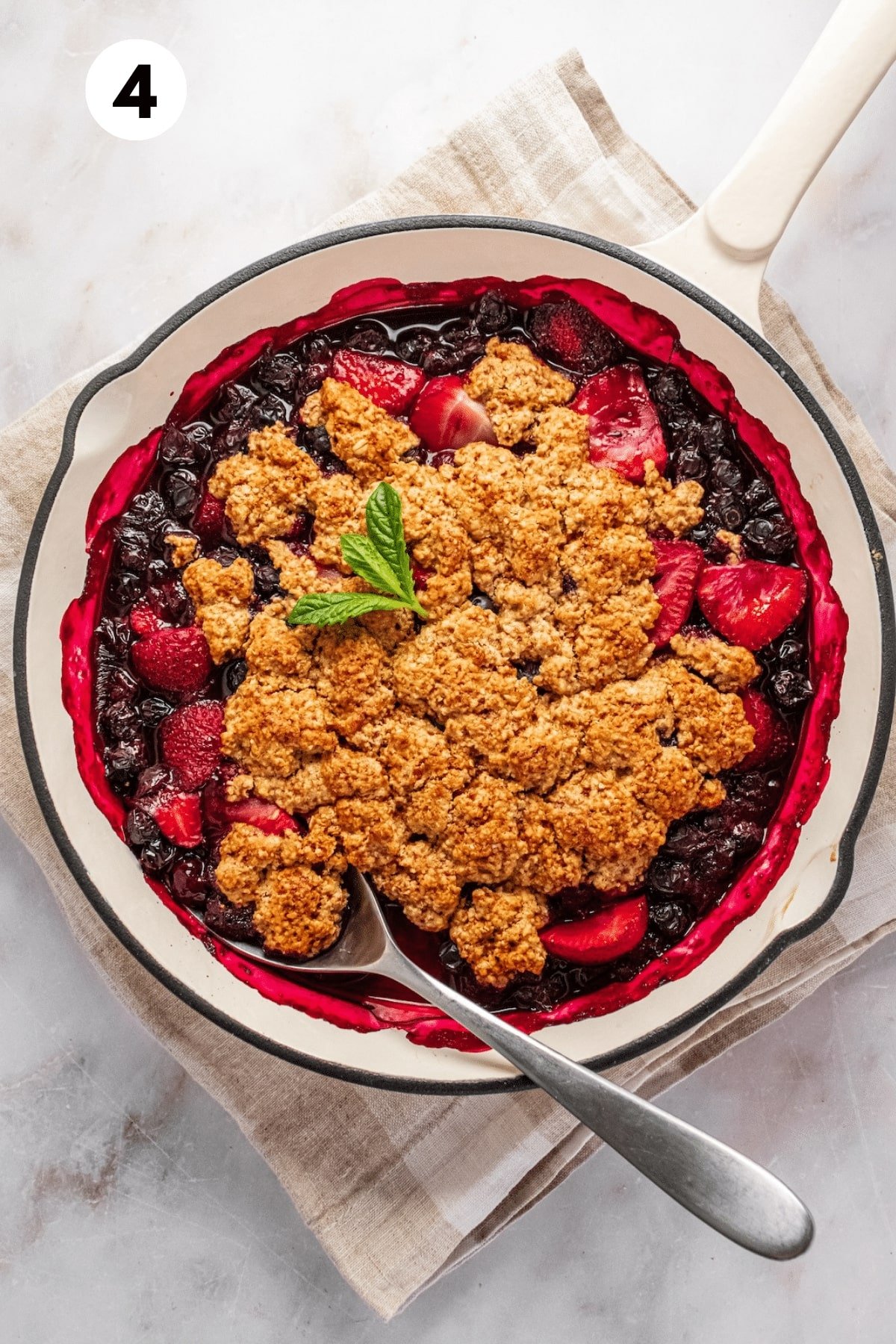 Gluten free berry cobbler garnished with mint and a spoon to the side.