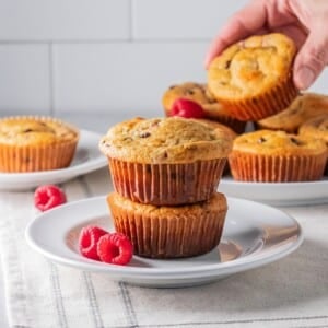 two muffins stacked on top of each other on a white plate with a hand picking up a muffin in the background.
