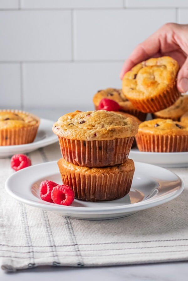 two muffins stacked on top of each other on a white plate with a hand picking up a muffin in the background.