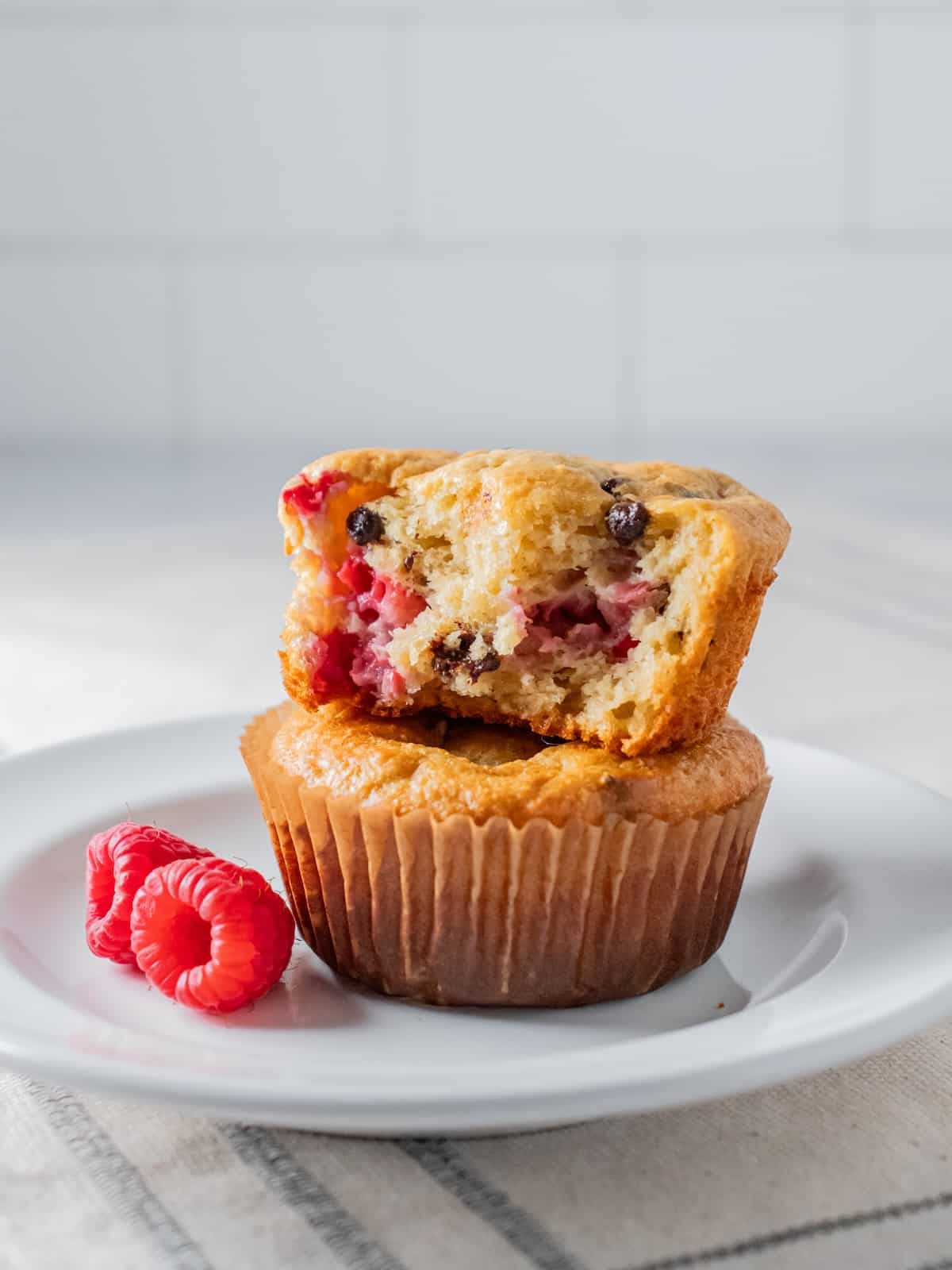 healthy raspberry chocolate chip muffin on a white plate with a bit out of it.
