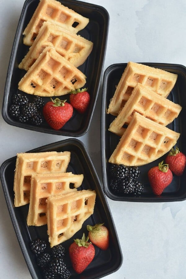 three waffles stacked in a meal prep container with strawberries and blueberries.