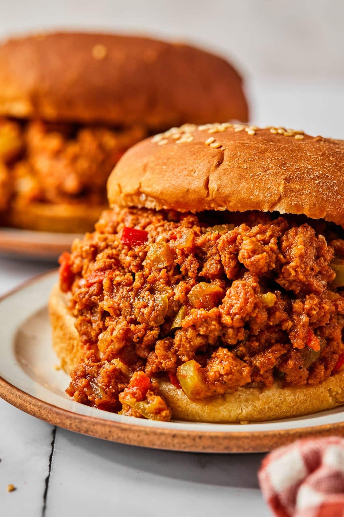 A crockpot sloppy joe served up on a plate stuffed inside a sesame seed bun.