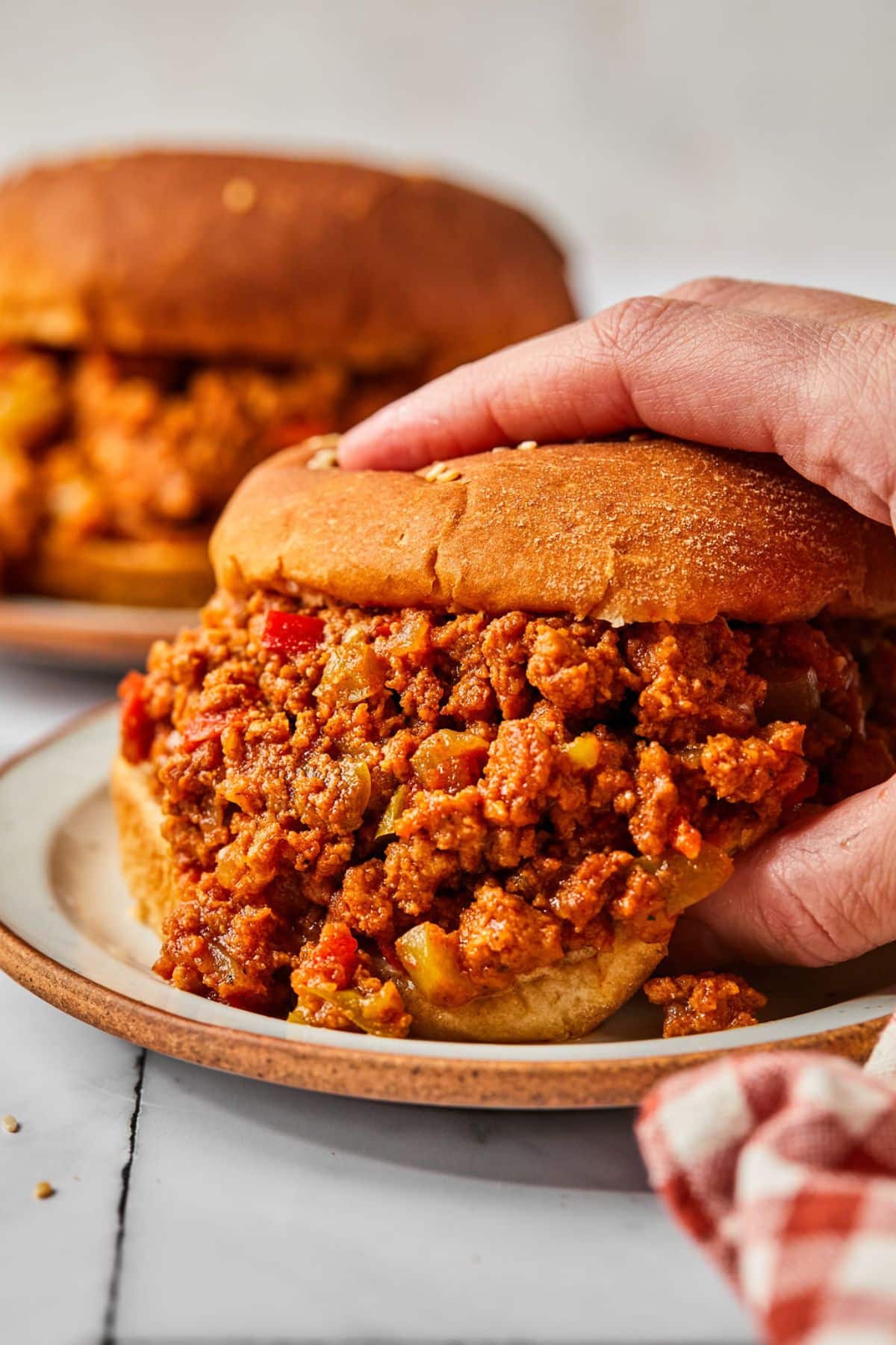 A hand reaching in to grab a turkey sloppy joe on the table with another in the background.