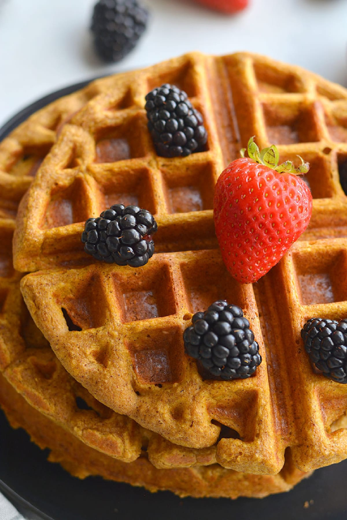 two waffles on a black plate with a strawberry on top and blackberries.