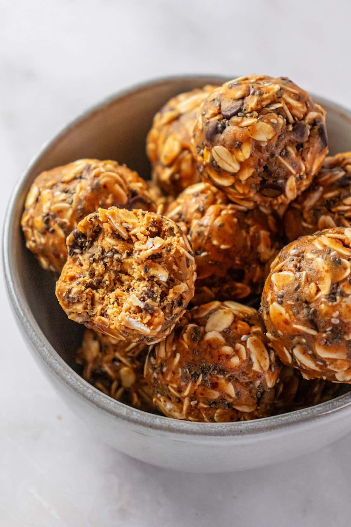 A bowl of almond butter energy balls with a bite taken from one on top. 
