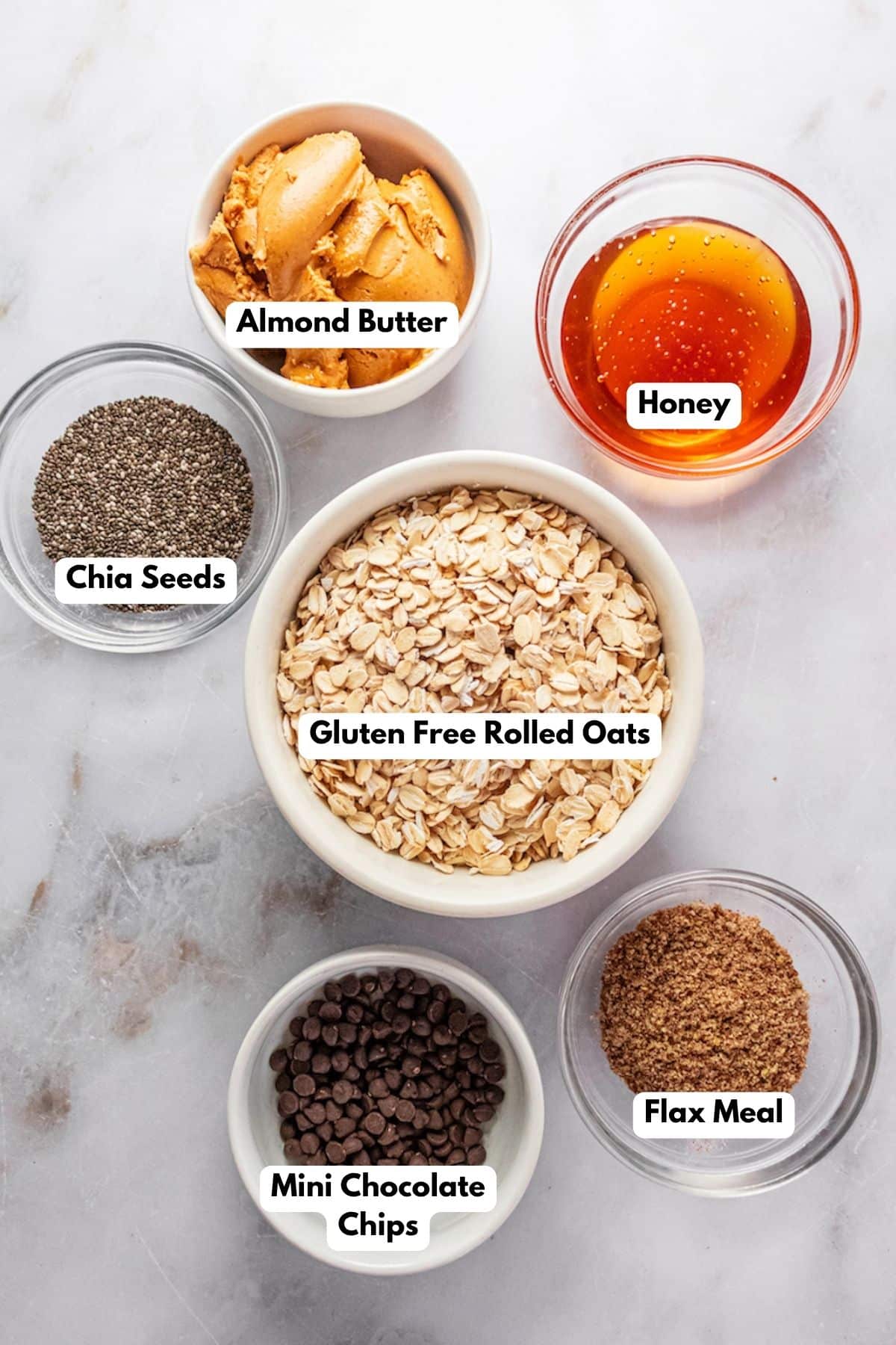 Ingredients to make almond butter protein balls in bowls with labels to identify each one.