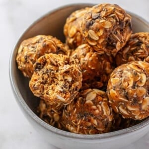 A bowl of almond butter protein balls with one on the top missing a bite.