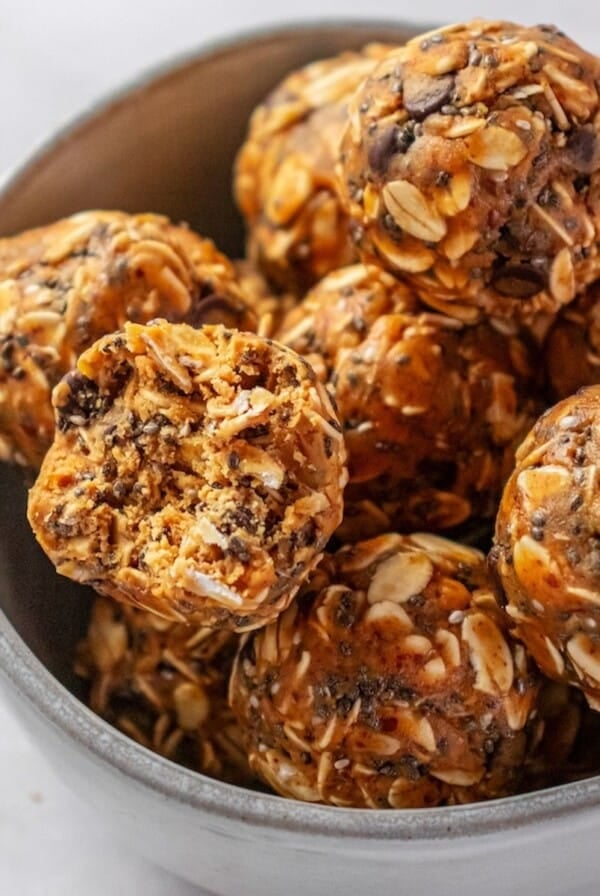 A bowl of almond butter protein balls with one on the top missing a bite.
