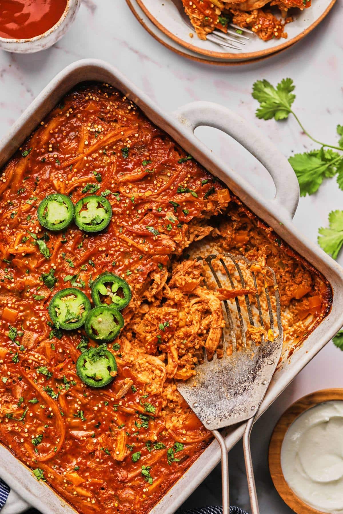 A casserole dish of healthy chicken enchilada casserole on the table garnished with sliced jalapenos. 