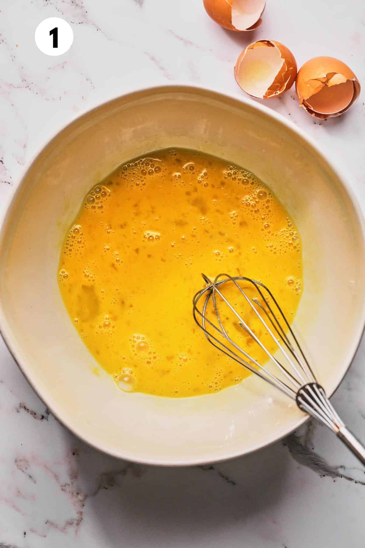 Eggs in a bowl with a whisk resting on the side.