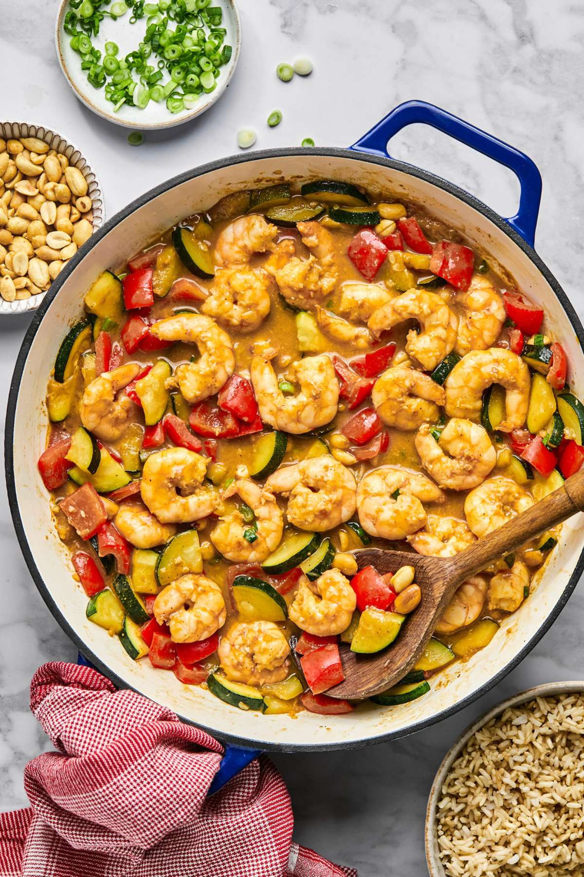 A skillet of kung pao shrimp with a wooden spoon digging in.