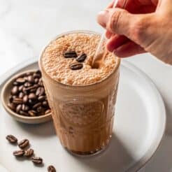 A mocha protein shake on a plate with a bowl of espresso beans to the side.