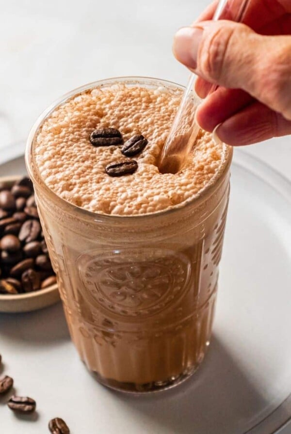 A mocha protein shake on a plate with a bowl of espresso beans to the side.